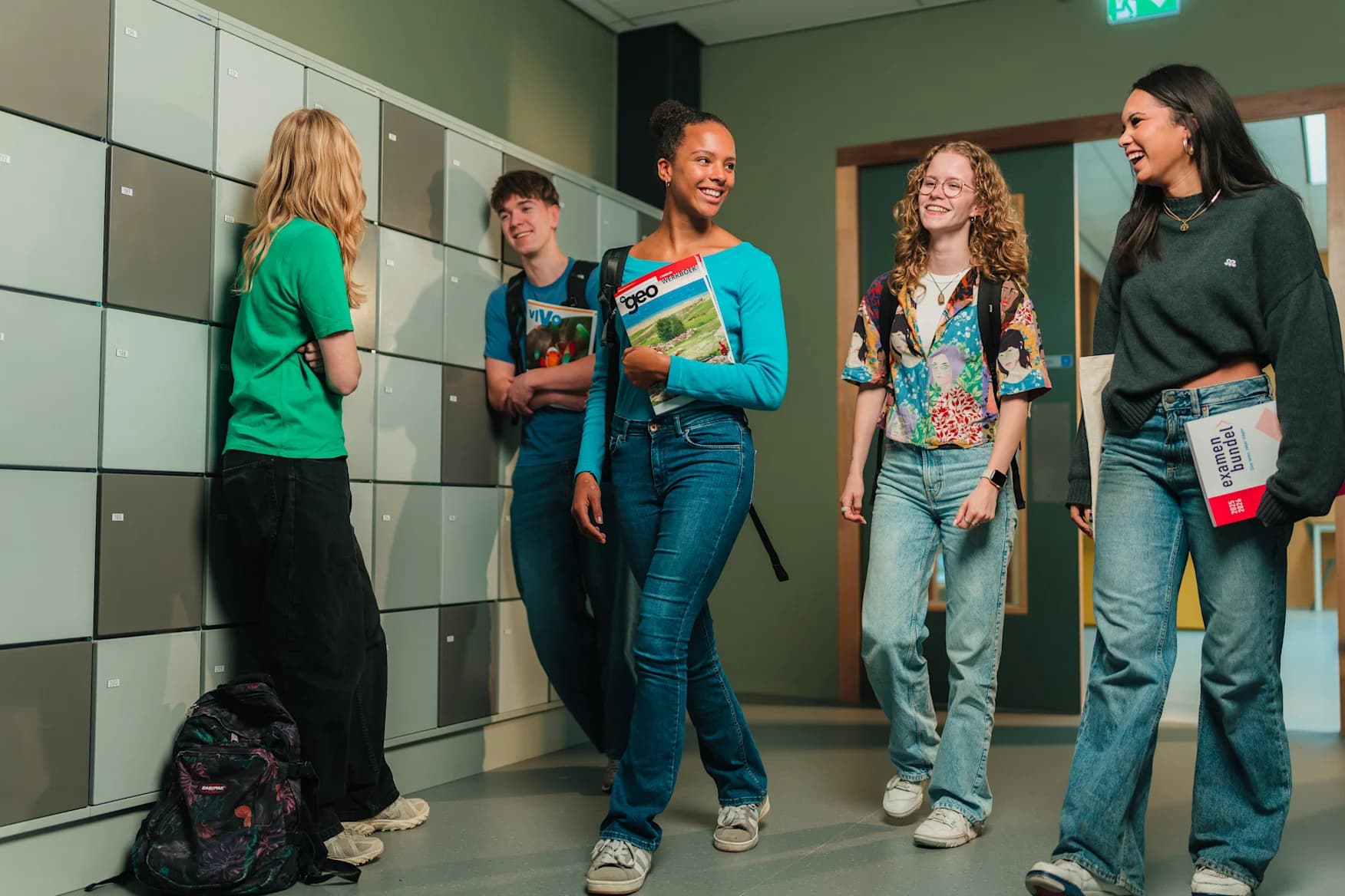Students in casual clothes smiling and walking down a school hallway, holding books and standing near lockers.
